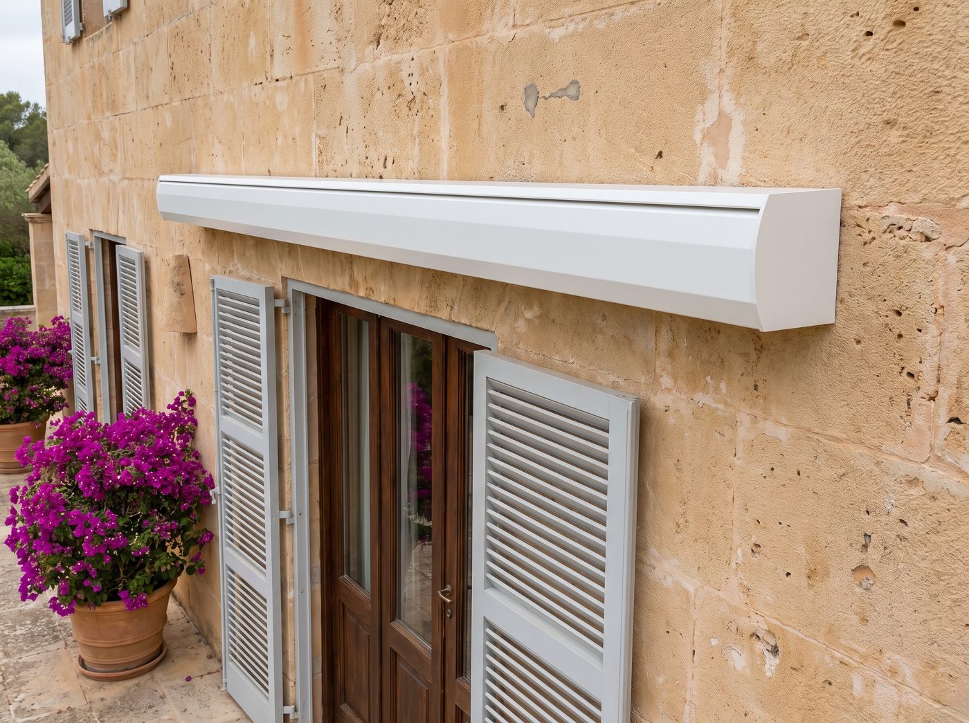 A retracted white cassette awning, its case closed on a limestone wall above French doors and shutters. Illustrative image
