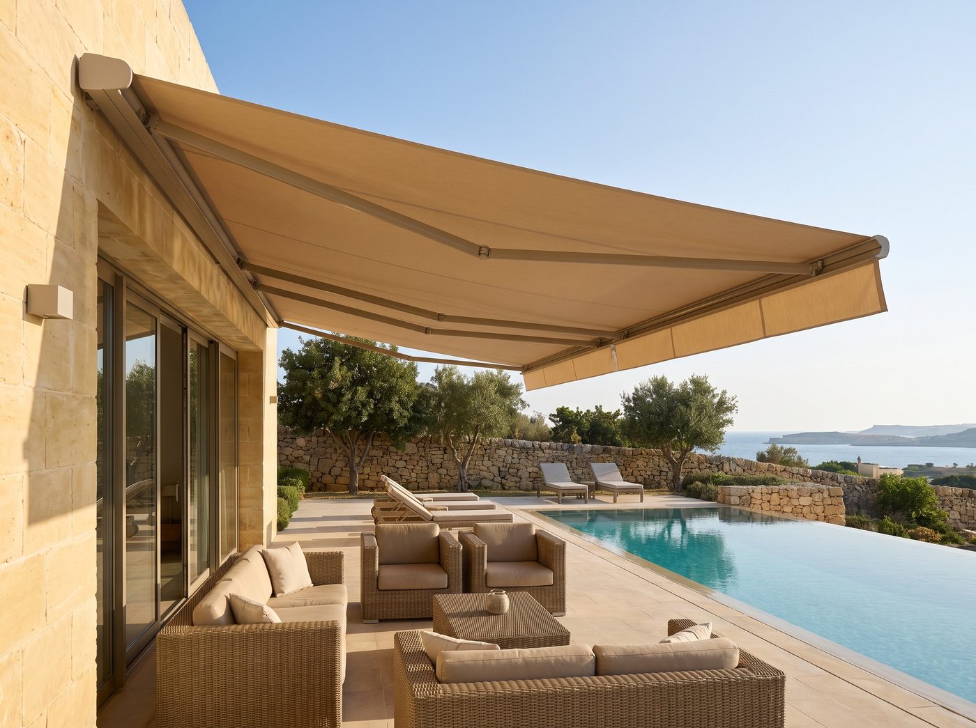 A wide sand-coloured cassette awning with a front valance over a lounge beside a villa pool. Illustrative image