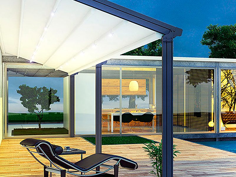 A pergola with a pleated white fabric roof over a deck and lounge chair at dusk