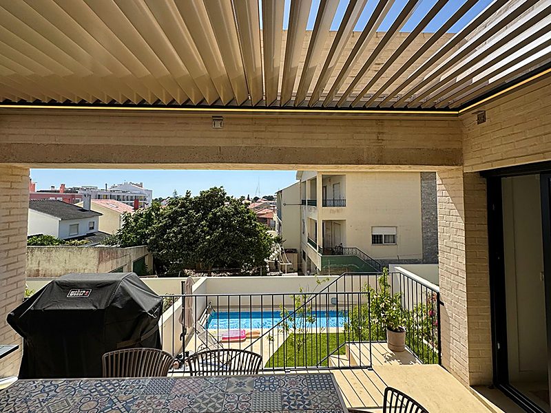 Looking up through open aluminium louvres over a covered terrace, with a garden pool beyond