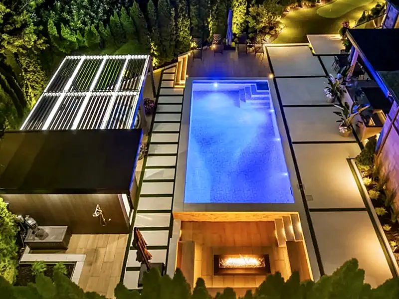 An aerial night view of a louvred pergola with LED lighting beside a lit pool