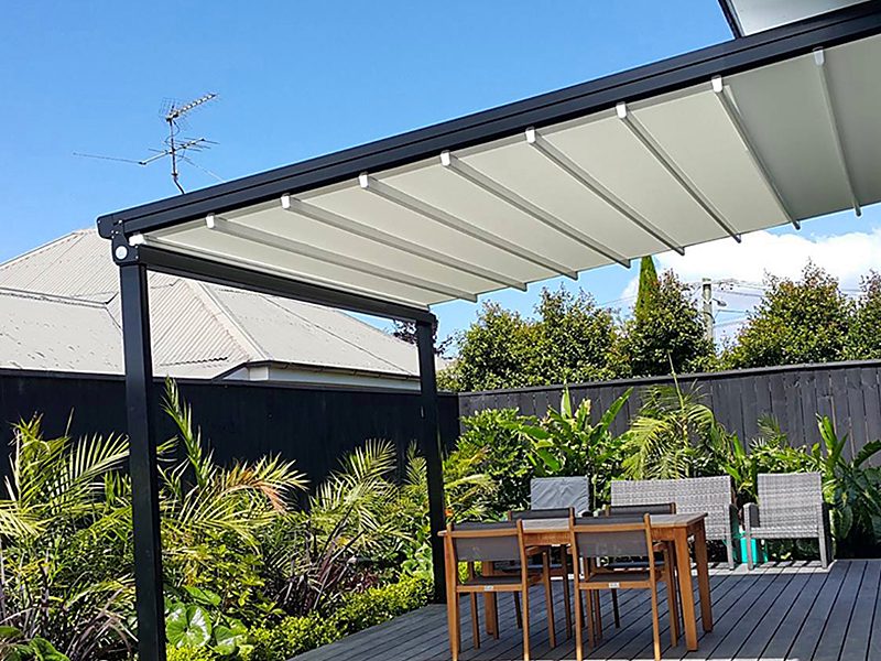 A dark-framed pergola with a white retractable fabric roof over a garden dining table