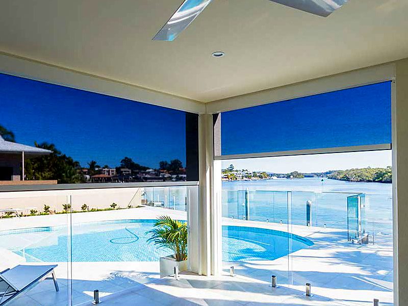 Two zip screens half lowered on a covered terrace, with a pool and the water beyond